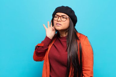 Latin kadın ciddi ve meraklı görünüyor, dinliyor, gizli bir konuşma veya dedikodu duymaya çalışıyor, kulak misafiri oluyor.