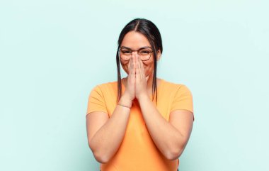 Latin kadın mutlu, neşeli, şanslı ve şaşkın görünüyor. İki eliyle ağzını kapatıyor.