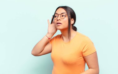 Latin kadın gülümsüyor, tuhaf bir şekilde yan tarafa bakıyor, dedikoduları dinlemeye ya da bir sırrı duymaya çalışıyor.