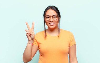 Latin kadın gülümsüyor ve arkadaş canlısı görünüyor. İki ya da iki numarayı gösteriyor. Elleri önde, geriye doğru sayıyor.