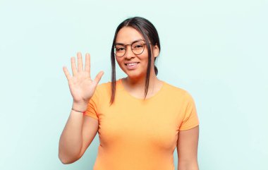 Latin bir kadın gülümsüyor ve arkadaş canlısı görünüyor, 5 ya da 5 numarayı gösteriyor, elleri önde, geriye doğru sayıyor.