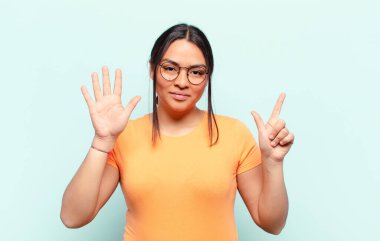 Latin bir kadın gülümsüyor ve dost canlısı görünüyor, 7 ya da 7 numarayı gösteriyor, eli önde, geri sayıyor.