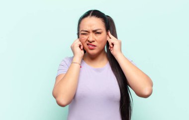 Kızgın, stresli ve sinirli görünen Latin bir kadın, iki kulağını da sağır edici bir sese, sese ya da gürültüye kapatıyor.