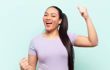 Latin kadın muzaffer bir şekilde bağırıyor, heyecanlı, mutlu ve şaşırmış görünüyor, kutlama yapıyor.