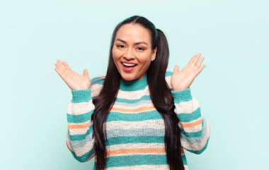 Latin kadın mutlu ve heyecanlı görünüyor. Beklenmedik bir sürprizle şoke olmuş. İki eli de açık.