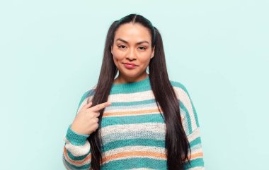 Latin kadın gururlu, kendinden emin ve mutlu görünüyor, gülümsüyor ve kendini işaret ediyor ya da bir numara işareti yapıyor.