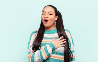 Latin kadın şok olmuş ve şaşırmış hissediyor, gülümsüyor, el ele tutuşuyor, o olmaktan mutlu ya da minnettarlık gösteriyor.