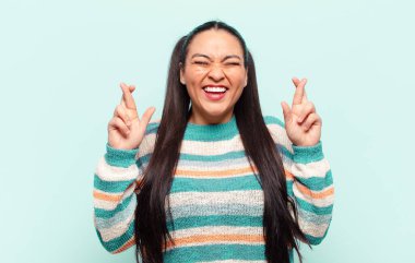 Latin kadın gülümsüyor ve endişeyle iki parmağını çapraz yapıyor. Endişeli ve iyi şanslar diliyor.