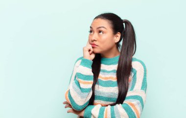 Yoğunlaşmış bakışlı, şüpheli bir ifadeyle, yukarı ve yana bakan Latin bir kadın.