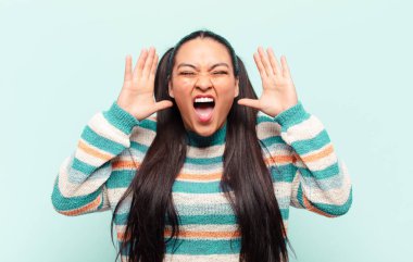 Panik ya da öfke içinde bağıran Latin bir kadın, şok olmuş, korkmuş ya da öfkeli, elleri başının yanında.