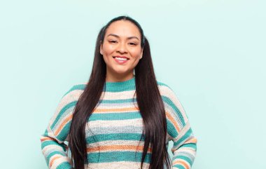 Latin kadın neşeli bir şekilde gülümsüyor. Olumlu, mutlu, kendinden emin ve rahat bir ifadeyle.