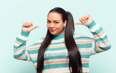 Latin kadın gururlu, kibirli ve kendinden emin, tatmin olmuş ve başarılı görünüyor, kendini işaret ediyor.