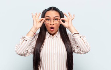 Latin kadın şaşkın, şaşkın ve şaşırmış hissediyor, elinde şaşkın, inançsız bir bakışla gözlük tutuyor.