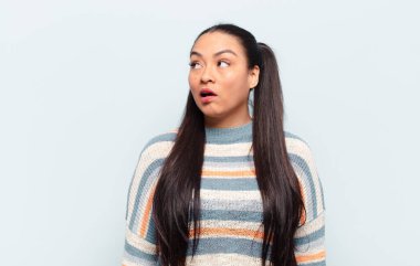 Latin kadın şaşkın, mutlu, şaşkın ve şaşırmış hissediyor, ağzı açık bir şekilde yana bakıyor.