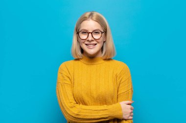 Sarışın kadın utangaç ve neşeli bir şekilde gülüyor, arkadaş canlısı ve olumlu ama güvensiz bir tavırla.