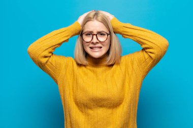 Sarışın kadın kendini stresli, endişeli, endişeli ya da korkmuş hissediyor. Elleri başının üstünde, hatayla panikliyor.