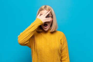 Sarışın kadın şok olmuş, korkmuş ya da korkmuş görünüyordu. Yüzü elle kaplıydı ve parmaklarının arasından bakıyordu.