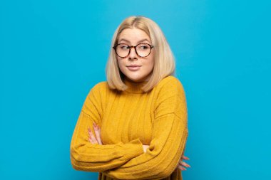 Sarışın kadın omuz silkiyor, kafası karışık ve kararsız, kolları bağlı ve şaşkın bir şekilde şüpheli bakıyor.