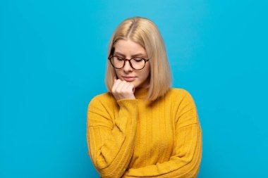 Sarışın kadın ciddi, düşünceli ve endişeli, elleri çenesine bastırılmış, yan bakıyor.