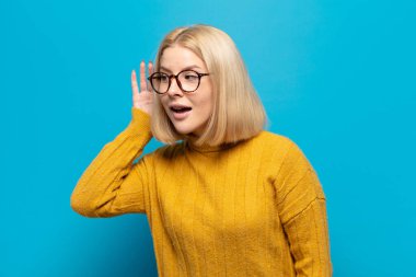 Sarışın kadın gülümsüyor, tuhaf bir şekilde yan tarafa bakıyor, dedikoduları dinlemeye ya da bir sırrı duymaya çalışıyor.