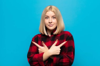 Sarışın kadın şaşkın ve şaşkın görünüyor, güvensiz ve şüpheyle zıt yönleri işaret ediyor.