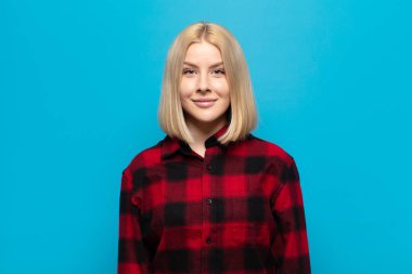 Sarışın kadın pozitif ve kendinden emin gülümsüyor. Tatmin olmuş, arkadaş canlısı ve mutlu görünüyor.