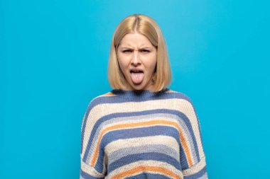 Sarışın kadın tiksinti ve tedirginlik duyuyor, dilini dışarı çıkarıyor, iğrenç ve iğrenç bir şeyden hoşlanmıyor.