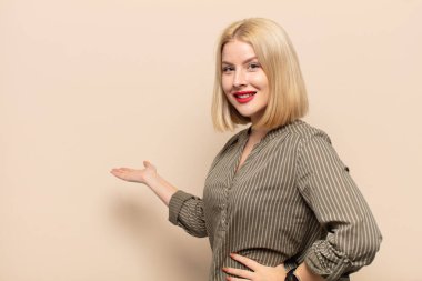 Sarışın kadın kendini mutlu ve neşeli hissediyor, gülümsüyor ve seni selamlıyor, dostça bir jestle içeri davet ediyor.