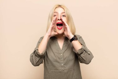 Sarışın kadın mutlu, heyecanlı ve pozitif hissediyor. Elleri ağızda, bağırarak bağırıyor.