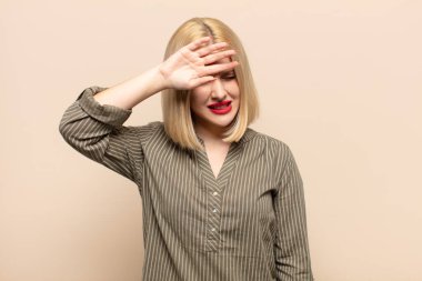 Sarışın kadın stresli, yorgun ve hayal kırıklığına uğramış, alnından ter damlıyor, umutsuz ve bitkin hissediyor.