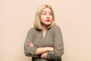 Sarışın kadın omuz silkiyor, kafası karışık ve kararsız, kolları bağlı ve şaşkın bir şekilde şüpheli bakıyor.