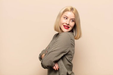 Sarışın kadın neşeyle gülümsüyor, mutlu, tatmin olmuş ve rahatlamış hissediyor, kollarını kavuşturup yan tarafa bakıyor.