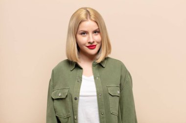 Sarışın kadın gururlu, kendinden emin, havalı, küstah ve küstah görünüyor, gülümsüyor, başarılı hissediyor.