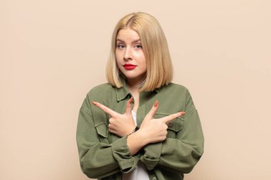 Sarışın kadın şaşkın ve şaşkın görünüyor, güvensiz ve şüpheyle zıt yönleri işaret ediyor.