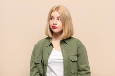 Sarışın kadın şaşkın ve şaşkın görünüyor, merak ediyor veya bir sorunu çözmeye çalışıyor veya düşünüyor.