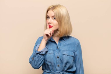 Sarışın kadın sessizlik ve sessizlik istiyor, parmağıyla ağzının önünde işaret ediyor, 