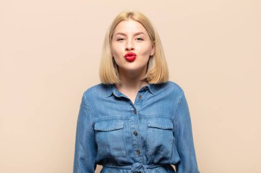 Sarışın kadın dudaklarını birbirine bastırıyor. Sevimli, eğlenceli, mutlu, sevimli bir yüz ifadesiyle. Öpücük gönderiyor.