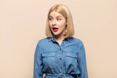 Sarışın kadın şaşkın, mutlu, şaşkın ve şaşırmış hissediyor, ağzı açık bir şekilde yana bakıyor.