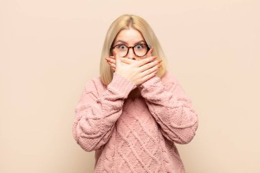 Sarışın kadın elleri ile ağzını kapatıyor, şok olmuş, şaşırmış bir ifadeyle, sır saklıyor ya da 