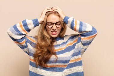 Sarışın kadın stresli ve hayal kırıklığına uğramış hissediyor, el ele tutuşuyor, yorgun, mutsuz ve migren ağrısı çekiyor.