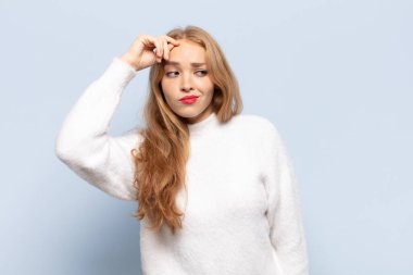 Sarışın kadın şaşkın ve şaşkın hissediyor, kafasını kaşıyor ve yan tarafa bakıyor.