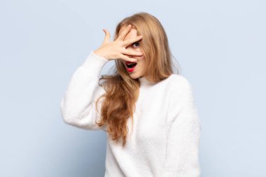 Sarışın kadın şok olmuş, korkmuş ya da korkmuş görünüyordu. Yüzü elle kaplıydı ve parmaklarının arasından bakıyordu.