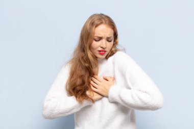 Sarışın kadın üzgün, incinmiş ve kalbi kırık görünüyor, iki elini de kalbe yakın tutuyor, ağlıyor ve depresyonda.