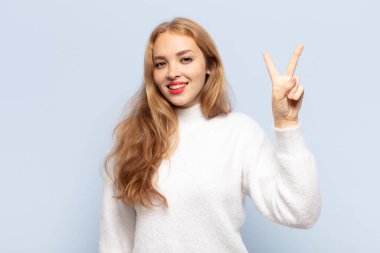 Sarışın kadın gülümsüyor ve arkadaş canlısı görünüyor. İki ya da iki numarayı gösteriyor. Elleri önde, geriye doğru sayıyor.