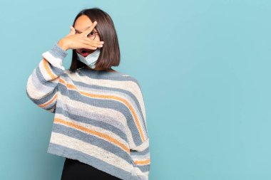 Genç İspanyol kadın şok olmuş, korkmuş ya da korkmuş görünüyor. Yüzü elle kaplanmış ve parmaklarının arasından gizlice bakıyor.