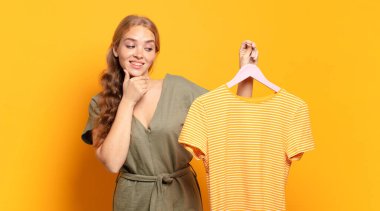 Mutlu, kendinden emin bir ifadeyle gülümsüyor, elleri çenesinde, merak ediyor ve yan tarafa bakıyor.