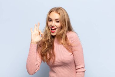 Sarışın kadın kendini başarılı ve tatmin olmuş hissediyor, ağzı açık gülümsüyor, elle işaret veriyor.