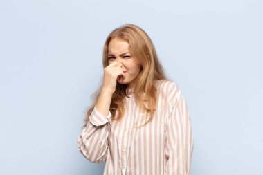 Sarışın kadın iğreniyor, kötü ve nahoş bir koku duymamak için burnunu tutuyor.