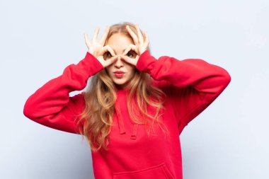 Şok olmuş, şaşırmış ve şaşırmış hisseden sarışın bir kadın, elinde şaşkın, inançsız bir bakışla gözlük tutuyor.