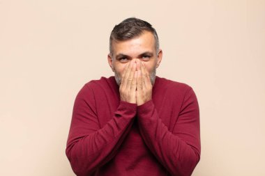 Yetişkin yakışıklı adam mutlu, neşeli, şanslı ve şaşkın görünüyor. İki eliyle ağzını kapatıyor.